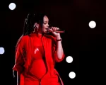 Rihanna performing on the Super Bowl Halftime Show stage in a colorful red jumpsuit.