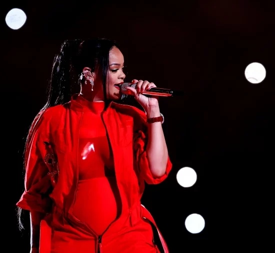 Rihanna performing on the Super Bowl Halftime Show stage in a colorful red jumpsuit.