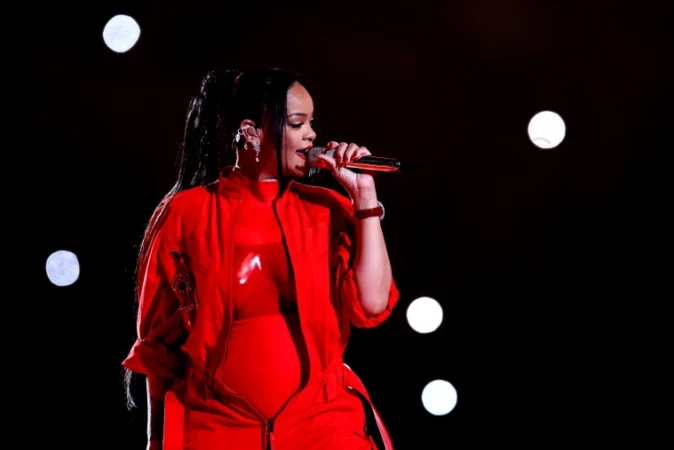 Rihanna performing on the Super Bowl Halftime Show stage in a colorful red jumpsuit.